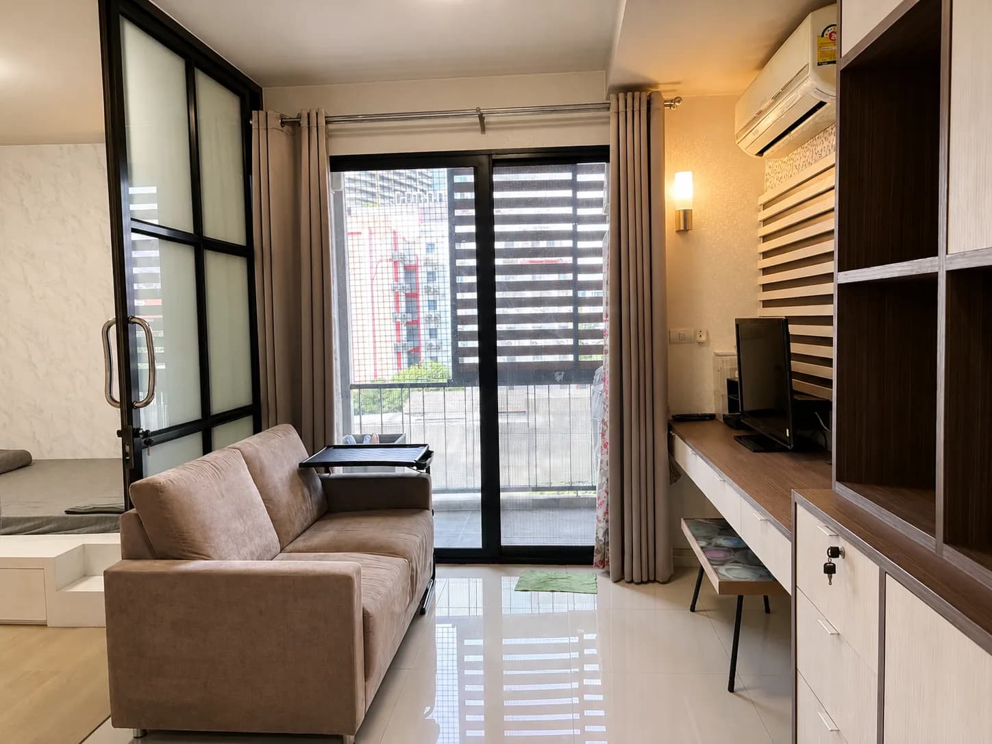 Living room view with sofa, TV wall, and natural light from the balcony